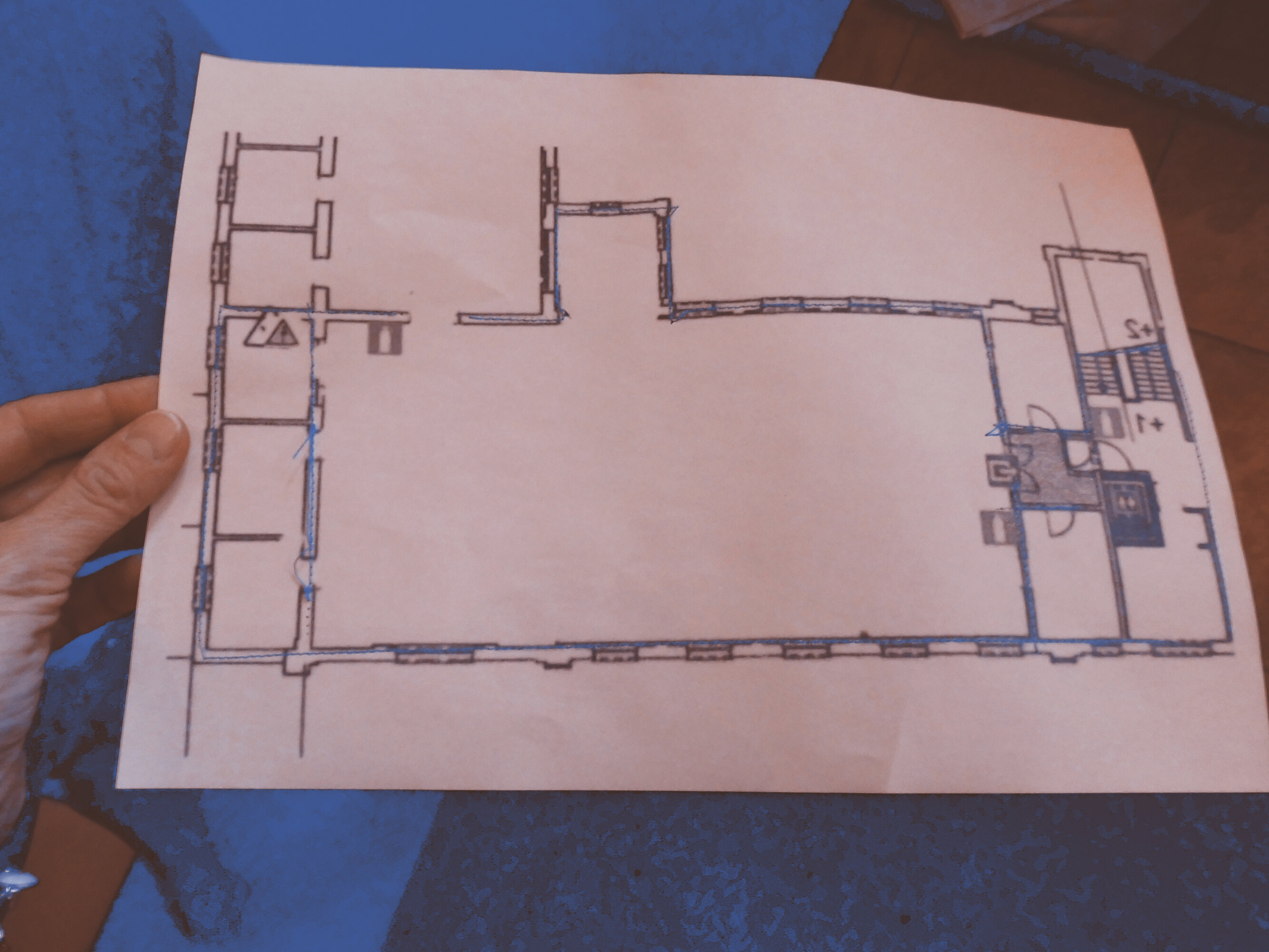 A hand is holding a sheet of paper. On it a map of a museum room is stitched with a dark thread.