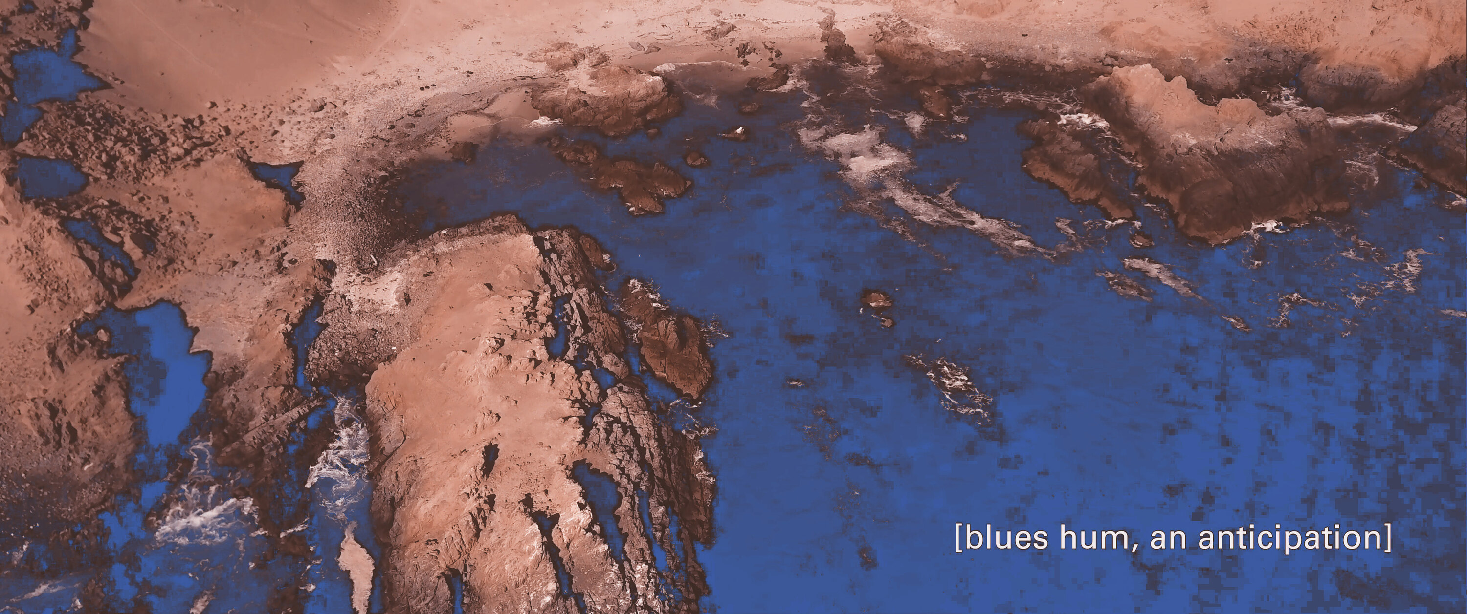 Screen capture from the movie: an aerial view of a coast, the dark sea meeting dusty rocky soil, with the caption “blues hum, an anticipation”