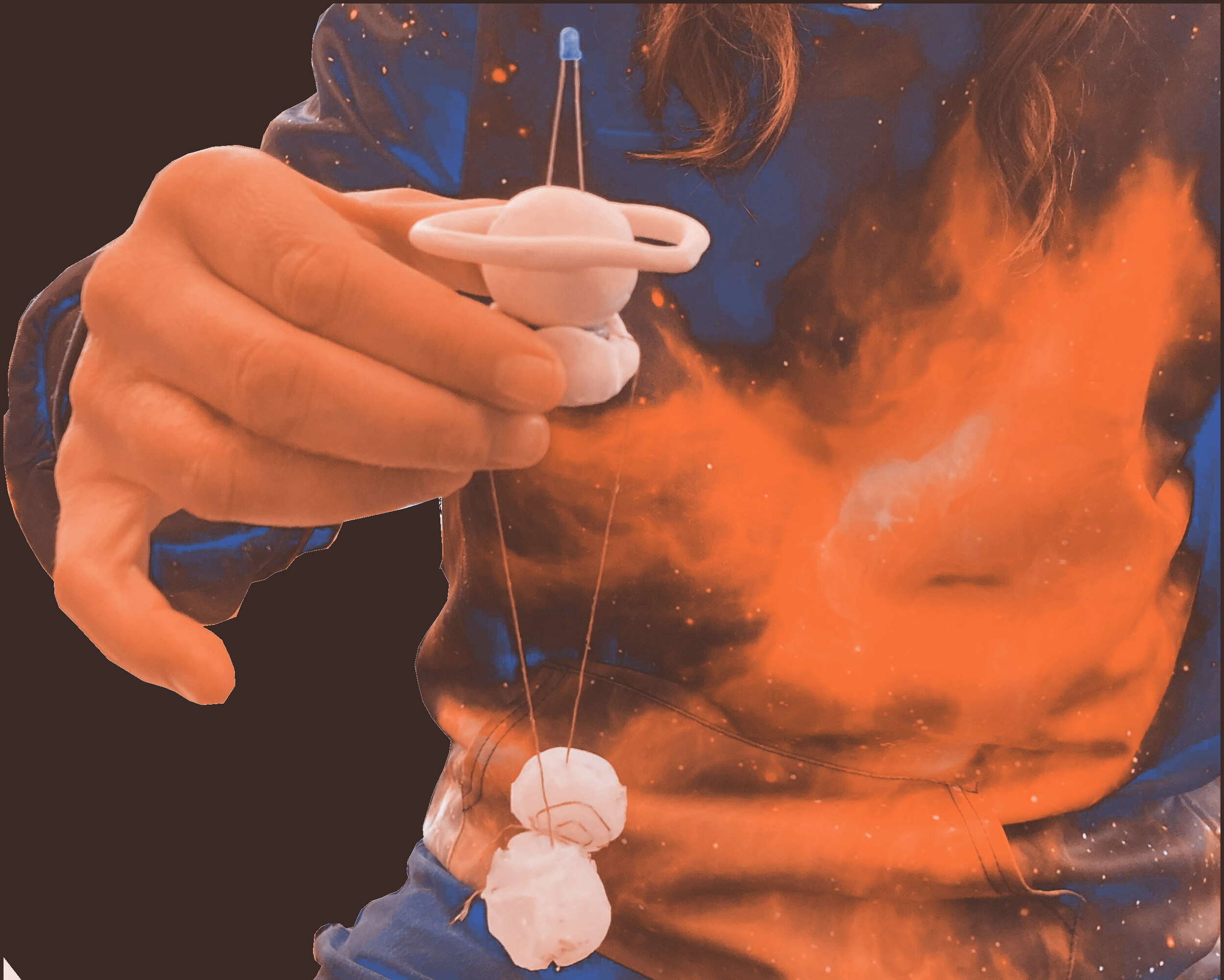 A planet like shape is being held by a hand. Two other celestial bodies are suspended from it, they are being held by a conductive thread. They are colliding.